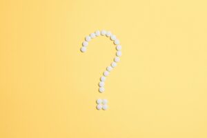 White pills arranged into a question mark shape on a vibrant yellow background for probiotic sibo
