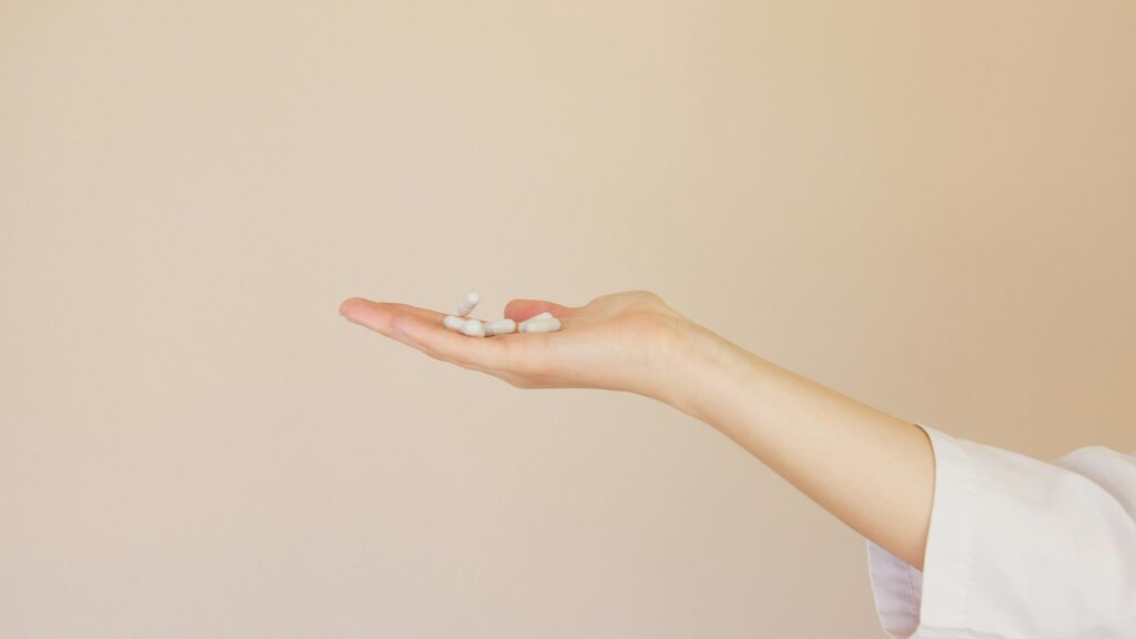 A female hand in a lab coat holds white capsules against a neutral background.