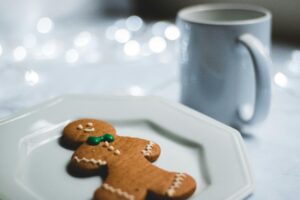 Festive gingerbread cookie on a plate, set against a soft bokeh backdrop with a mug, evoking holiday warmth.